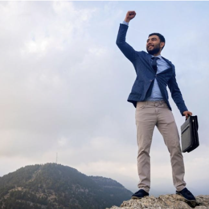 A person in business attire standing confidently on a rocky peak, holding a briefcase and raising a fist triumphantly. The scene conveys themes of overcoming challenges and transforming insecurity into an advantage.