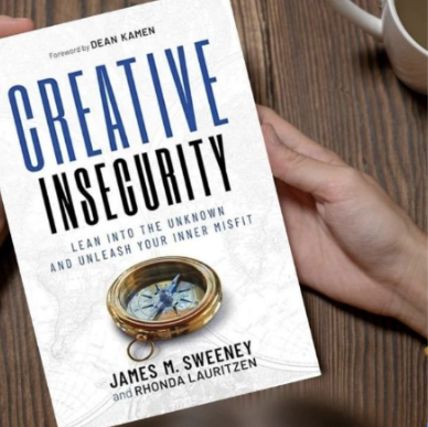 A hand holding a book titled "Creative Insecurity," authored by James M. Sweeney and Rhonda Lauritzen. The book's subtitle emphasizes the use of insecurity as a tool for personal growth, with a compass symbol adding a metaphorical layer of navigating challenges.