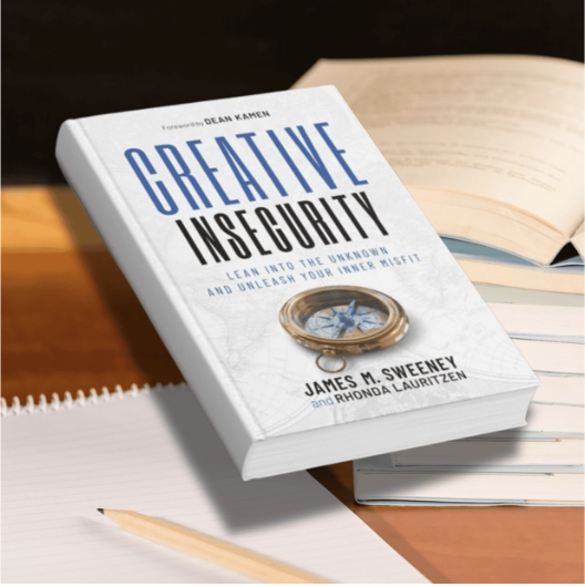 A hardcover copy of the book Creative Insecurity, written for entrepreneurs by serial entrepreneur James M. Sweeney and Rhonda Lauritzen, floats on a desk beside open notebooks.